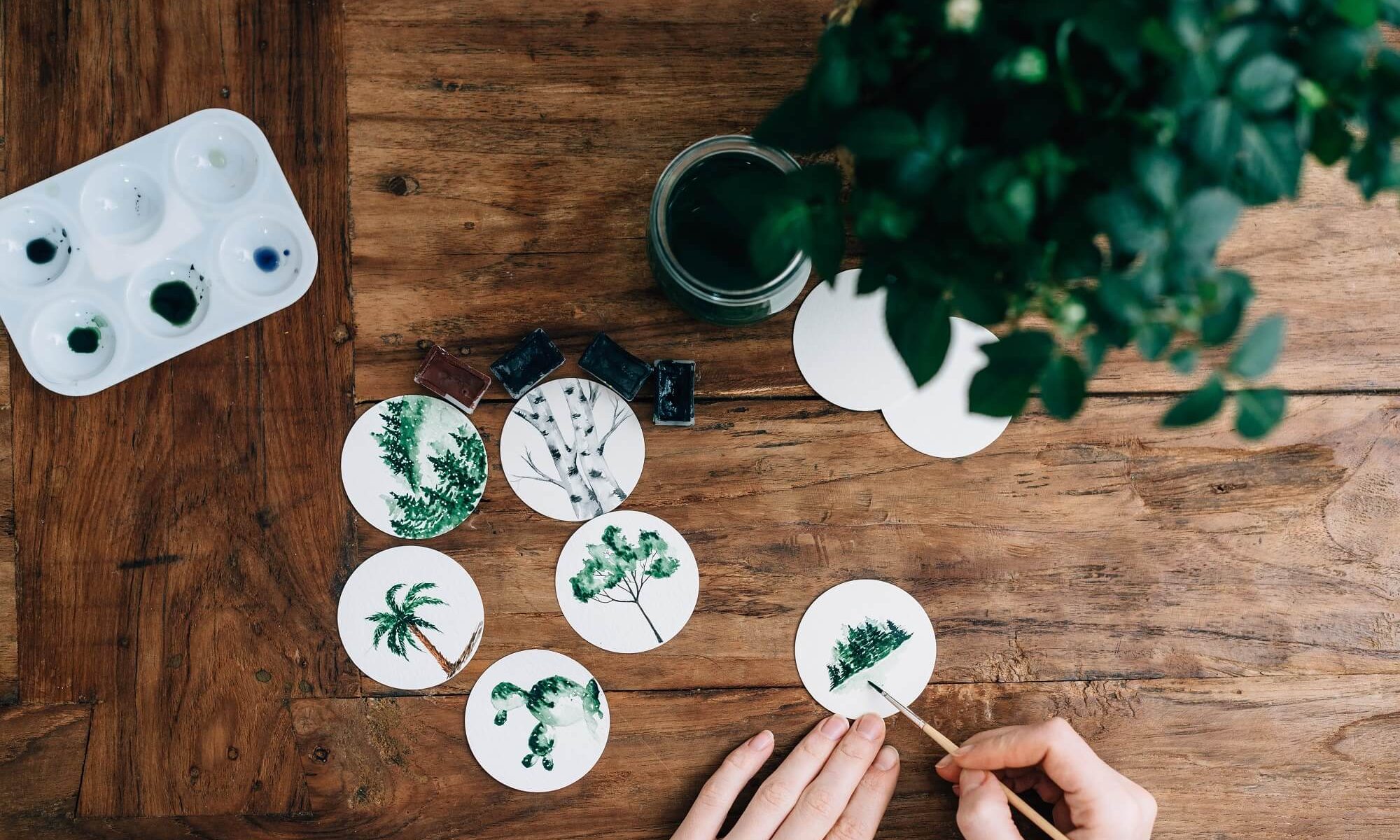 mesa de madeira com uma mão pintando árvores verdes com pincel