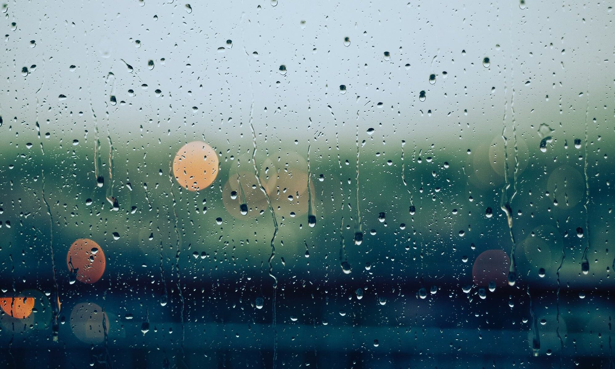 chuva caindo no vidro com luzes desfocadas ao fundo